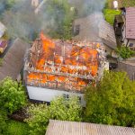 Luftaufnahme eines brennenden Hauses mit orangefarbenen Flammen und weißem, dickem Rauch